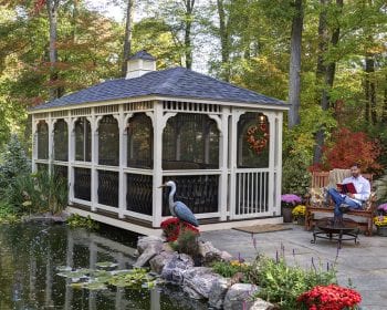 Baroque style ivory vinyl gazebo cupola with screens on a patio by a pond.