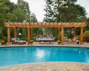 Artisan cedar pergola on a stone patio by the pool.
