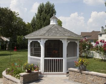 White octagonal country style gazebo with screens on a backyard patio.