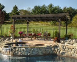 Brown hearthside pergola on a stone patio by a pool.