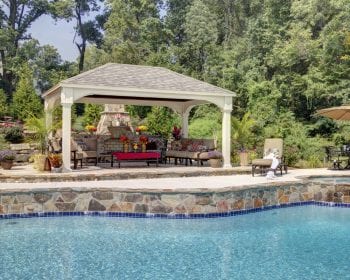 Patio furniture and fire place underneath a traditional ivory vinyl pavilion by the pool.