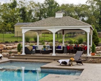 Wicker furniture underneath a traditional white vinyl pavilion on a patio by the pool.