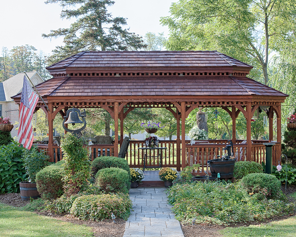 Oval New England style wood gazebo with a cedar pagoda roof in a garden.