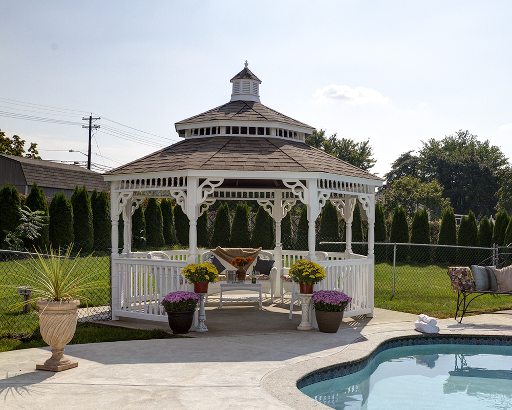 White octagonal colonial style gazebo with a brown pagoda roof by a pool.