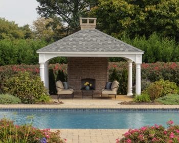 Traditional white vinyl pavilion with a fire place on a brick patio by the pool.