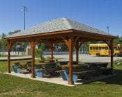 Traditional brown wood pavilion at a park with picnic benches underneath.