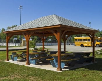 Traditional brown wood pavilion at a park with picnic benches underneath.