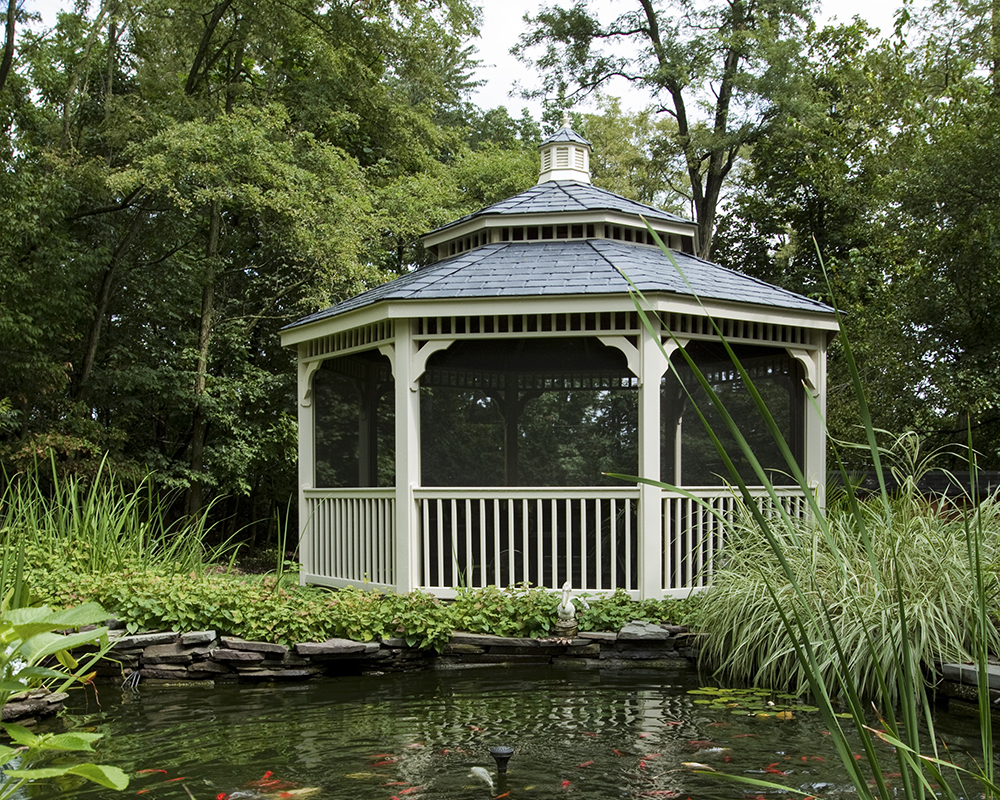 Ivory octagonal country style vinyl gazebo with a gray pagoda roof by a pond.