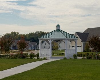 White octagonal country style vinyl gazebo with a green metal roof in a park.