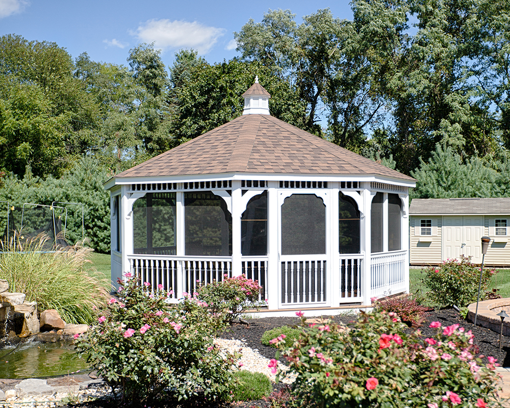 White octagonal vinyl gazebo with screens in a backyard garden.