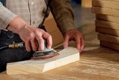 A closeup of a carpenter's hands sanding a piece of wood.