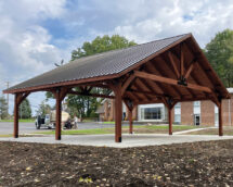 Country Lane Wooden Palatian Pavilion on a white concrete slab with brown mulch surrounding.